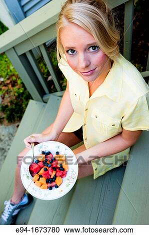 Portrait of a 20 year old blond woman in casual workout clothing sitting on steps of a house holding a bowl of fresh mixed fruit View Large Photo Image Stock Image - Portrait of a 20 year old blond woman in casual workout clothing sitting on steps of a house holding a bowl of fresh mixed fruit. Fotosearch