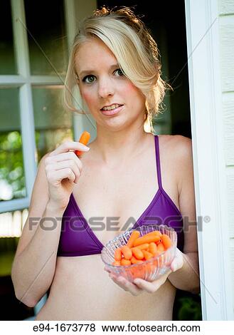 Portrait of a 20 year old blond woman in casual workout clothing standing a doorway of a house holding a bowl of carrots View Large Photo Image Stock Photo - Portrait of a 20 year old blond woman in casual workout clothing standing a doorway of a house holding a bowl of carrots. Fotosearch