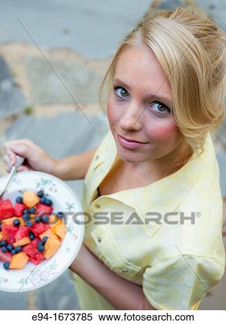 Portrait of a 20 year old blond woman in casual workout clothing standing on a porch of a house holding a bowl of fresh mixed fruit View Large Photo Image Stock Photography - Portrait of a 20 year old blond woman in casual workout clothing standing on a porch of a house holding a bowl of fresh mixed fruit. Fotosearch