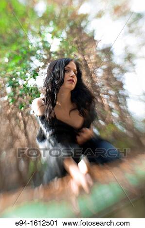 Portrait of a 20 year old brunettte woman in jeans and a black top kneeling on an old car in a forest setting View Large Photo Image Stock Image - Portrait of a 20 year old brunettte woman in jeans and a black top kneeling on an old car in a forest setting. Fotosearch