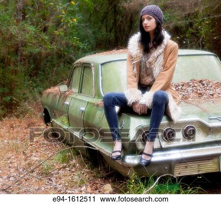 Portrait of a 20 year old brunettte woman wearing a knit hat and a leather coat sitting on an old car in a forest setting View Large Photo Image Stock Image - Portrait of a 20 year old brunettte woman wearing a knit hat and a leather coat sitting on an old car in a forest setting. Fotosearch