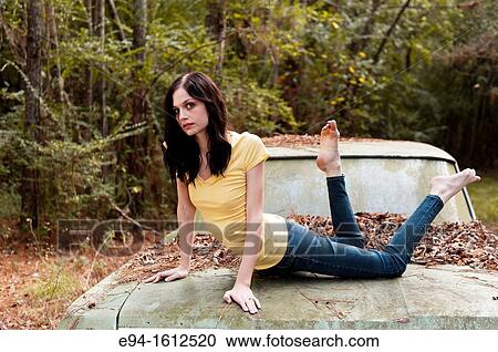 Portrait of a 20 year old brunettte woman lying on the trunk lit of an old car in a forest setting View Large Photo Image Stock Image - Portrait of a 20 year old brunettte woman lying on the trunk lit of an old car in a forest setting. Fotosearch