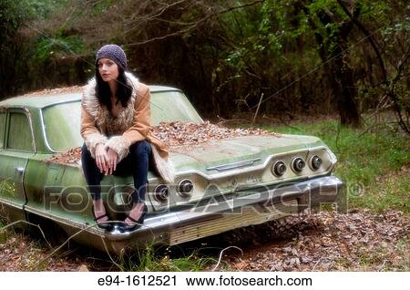Portrait of a 20 year old brunettte woman wearing a knit hat and a leather coat sitting on an old car in a forest setting View Large Photo Image Stock Image - Portrait of a 20 year old brunettte woman wearing a knit hat and a leather coat sitting on an old car in a forest setting. Fotosearch