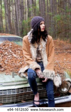Portrait of a 20 year old brunettte woman wearing a knit hat and a leather coat sitting on an old car in a forest setting View Large Photo Image Stock Image - Portrait of a 20 year old brunettte woman wearing a knit hat and a leather coat sitting on an old car in a forest setting. Fotosearch