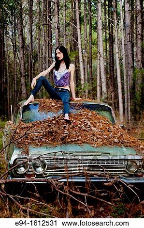 Portrait of a 20 year old brunettte woman in jeans sitting on the roof of on an old car in a forest setting. View Large Photo Image Stock Image - Portrait of a 20 year old brunettte woman in jeans sitting on the roof of on an old car in a forest setting.. Fotosearch