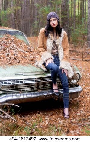 Portrait of a 20 year old brunettte woman wearing a knit hat and a leather coat sitting on an old car in a forest setting View Large Photo Image Stock Photo - Portrait of a 20 year old brunettte woman wearing a knit hat and a leather coat sitting on an old car in a forest setting. Fotosearch