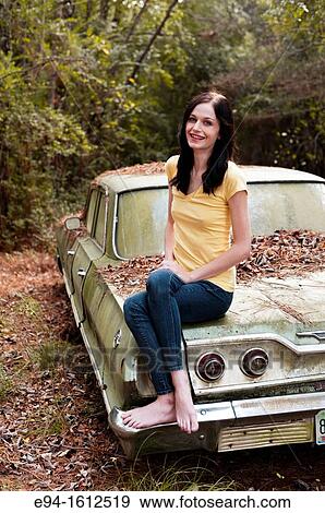 Portrait of a 20 year old brunettte woman sitting on an old car in a forest setting View Large Photo Image Stock Photo - Portrait of a 20 year old brunettte woman sitting on an old car in a forest setting. Fotosearch