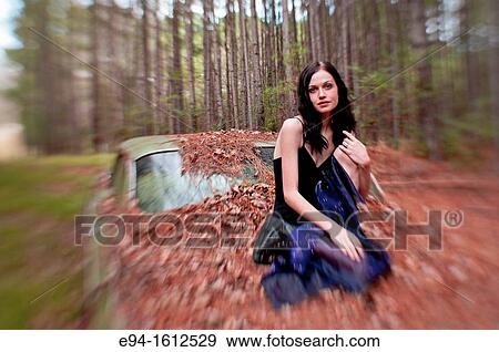 Portrait of a 20 year old brunettte woman sitting on an old car in a forest setting View Large Photo Image Stock Photo - Portrait of a 20 year old brunettte woman sitting on an old car in a forest setting. Fotosearch