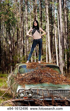 Portrait of a 20 year old brunettte woman in jeans standing on an old car in a forest setting View Large Photo Image Stock Photograph - Portrait of a 20 year old brunettte woman in jeans standing on an old car in a forest setting. Fotosearch