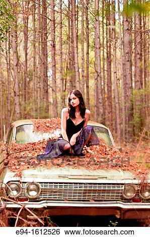 Portrait of a 20 year old brunettte woman sitting on an old car in a forest setting View Large Photo Image Stock Photograph - Portrait of a 20 year old brunettte woman sitting on an old car in a forest setting. Fotosearch