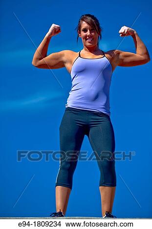 Picture - Portrait of a 23 year old brunette woman in workout clothing outdoors flexing her arms. Fotosearch
