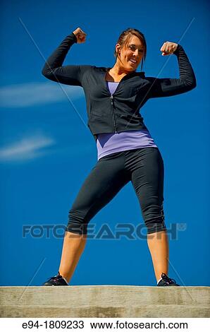 Portrait of a 23 year old brunette woman in workout clothing outdoors flexing her arms View Large Photo Image Stock Image - Portrait of a 23 year old brunette woman in workout clothing outdoors flexing her arms. Fotosearch