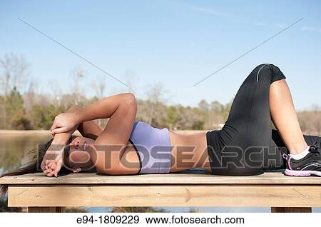 Portrait of a 23 year old brunette woman in workout clothing lying on a bench peaking at the camera View Large Photo Image Stock Photo - Portrait of a 23 year old brunette woman in workout clothing lying on a bench peaking at the camera. Fotosearch