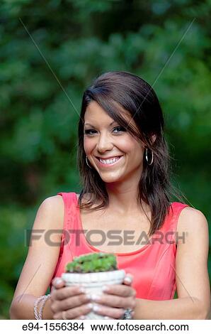 Portrait of a 25 year old brunette woman in a sleeveless dress in an outdoor garden setting holding a small Sempervivum, Hen & Chicks plant. View Large Photo Image Picture - Portrait of a 25 year old brunette woman in a sleeveless dress in an outdoor garden setting holding a small Sempervivum, Hen & Chicks plant.. Fotosearch