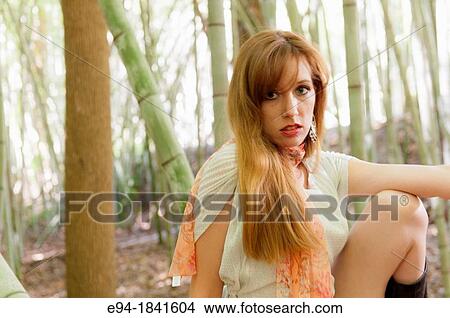 Picture - Portrait of a 30 year old redheaded woman wearing a white dress in a bamboo forest. Fotosearch