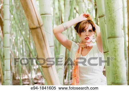 Stock Photography - Portrait of a 30 year old redheaded woman wearing a white dress in a bamboo forest. Fotosearch