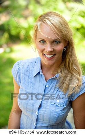 Portrait of a 35 year old blond woman wearing a blue blouse and jeans in a garden setting looking at the camera View Large Photo Image Picture - Portrait of a 35 year old blond woman wearing a blue blouse and jeans in a garden setting looking at the camera. Fotosearch