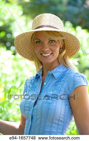 Stock Photo - Portrait of a 35 year old blond woman wearing a straw hat and a blue blouse in a garden setting. Fotosearch