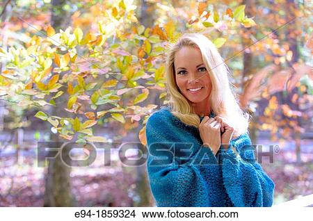 Picture - Portrait of a 38 year old blond woman wearing a sweater looking at the camera in a forest setting in the fall. Fotosearch