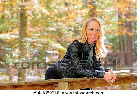Portrait of a 38 year old blond woman smiling at the camera leaning on the railing of a foot bridge in a forest setting in the fall View Large Photo Image Stock Photo - Portrait of a 38 year old blond woman smiling at the camera leaning on the railing of a foot bridge in a forest setting in the fall. Fotosearch
