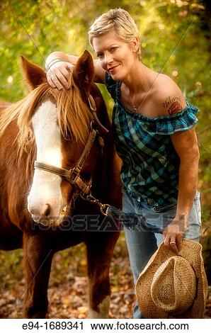 Portrait of a 41 year old blond woman wearing blue jeans walking with a horse in a country setting View Large Photo Image Stock Image - Portrait of a 41 year old blond woman wearing blue jeans walking with a horse in a country setting. Fotosearch