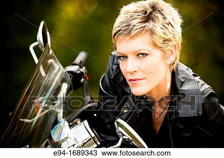 Portrait of a 41 year old blond woman looking at the camera leaning on a motorcycle View Large Photo Image Stock Image - Portrait of a 41 year old blond woman looking at the camera leaning on a motorcycle. Fotosearch
