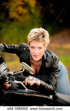 Portrait of a 41 year old blond woman looking at the camera leaning on a motorcycle View Large Photo Image Stock Image - Portrait of a 41 year old blond woman looking at the camera leaning on a motorcycle. Fotosearch