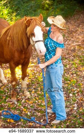 Portrait of a 41 year old blond woman wearing blue jeans walking with a horse in a country setting View Large Photo Image Stock Photo - Portrait of a 41 year old blond woman wearing blue jeans walking with a horse in a country setting. Fotosearch