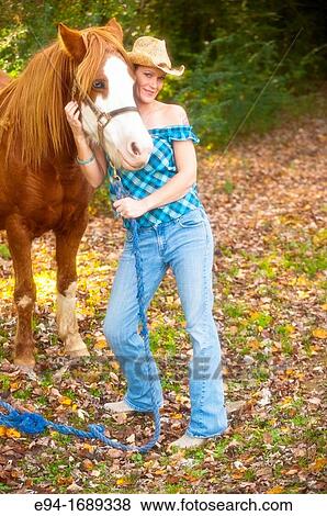 Portrait of a 41 year old blond woman wearing blue jeans walking with a horse in a country setting View Large Photo Image Stock Photo - Portrait of a 41 year old blond woman wearing blue jeans walking with a horse in a country setting. Fotosearch