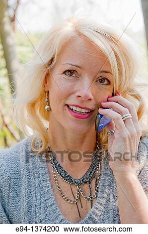 Portrait of a 44 year old blond woman talking on a mobile phone, outdoors View Large Photo Image Stock Image - Portrait of a 44 year old blond woman talking on a mobile phone, outdoors. Fotosearch