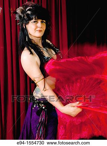 Stock Image - Portrait of a 45 year old brunette woman in an exotic costume waving red fabric. Fotosearch