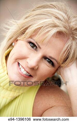 Stock Photograph - Portrait of a 50 year old blond woman in an outdoor setting smiling at the camera. Fotosearch