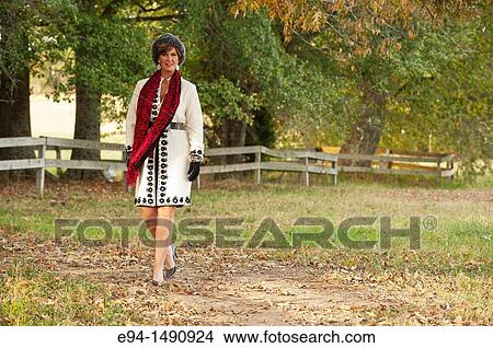 Portrait of a 52 year old blonde woman dressed in a white winter coat with a hat and a scarf in a country setting looking at the camera. View Large Photo Image Picture - Portrait of a 52 year old blonde woman dressed in a white winter coat with a hat and a scarf in a country setting looking at the camera.. Fotosearch