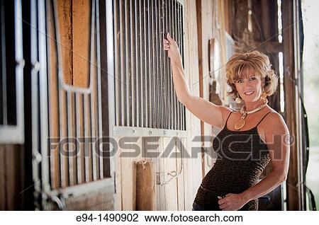 Stock Image - Portrait of a 52 year old blonde woman in casual clothing in a horse barn setting looking at the camera.. Fotosearch
