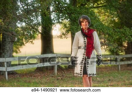 Stock Image - Portrait of a 52 year old blonde woman dressed in a white winter coat with a hat and a scarf in a country setting looking at the camera.. Fotosearch