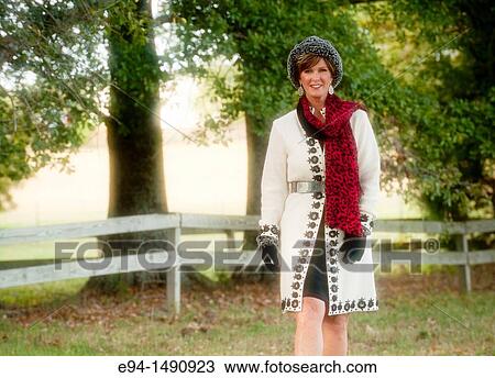 Portrait of a 52 year old blonde woman dressed in a white winter coat with a hat and a scarf in a country setting looking at the camera. View Large Photo Image Stock Image - Portrait of a 52 year old blonde woman dressed in a white winter coat with a hat and a scarf in a country setting looking at the camera.. Fotosearch
