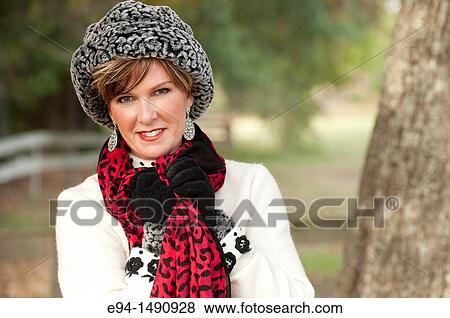 Stock Photo - Portrait of a 52 year old blonde woman dressed in a white winter coat with a hat and a scarf in a country setting looking at the camera.. Fotosearch