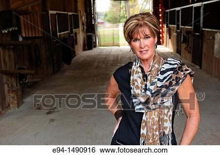 Portrait of a 52 year old blonde woman in casual black dress in a horse barn setting looking at the camera. View Large Photo Image Stock Photograph - Portrait of a 52 year old blonde woman in casual black dress in a horse barn setting looking at the camera.. Fotosearch