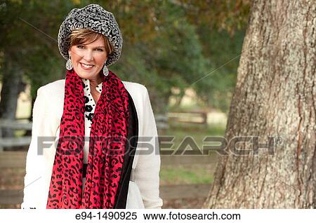 Stock Photography - Portrait of a 52 year old blonde woman dressed in a white winter coat with a hat and a scarf in a country setting looking at the camera.. Fotosearch