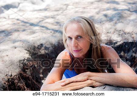Stock Image - Portrait of a 57 year old woman on a beach looking at the camera. Fotosearch