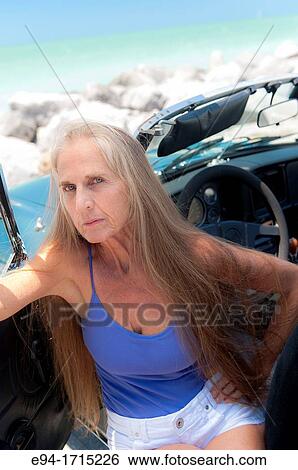 Stock Photograph - Portrait of a 57 year old woman sitting in her MG car at a beach. Fotosearch