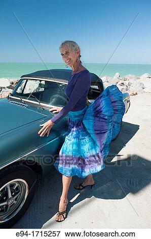 Portrait of a 57 year old woman standing by her MG car at a beach Stock