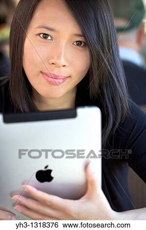 Stock Photograph - Portrait of a beautiful Asian woman holding an iPad. Fotosearch