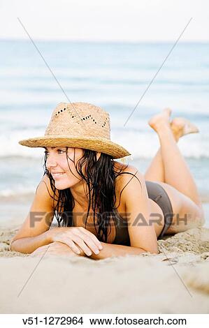 Picture - Portrait of a beautiful brunette woman at the beach with a bikini and a hat. Fotosearch