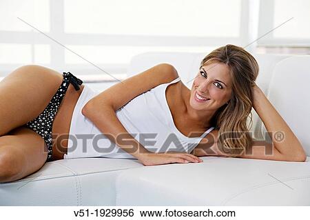 Stock Photograph - Portrait of a blonde pretty woman smiling at camera at the sofa. Fotosearch