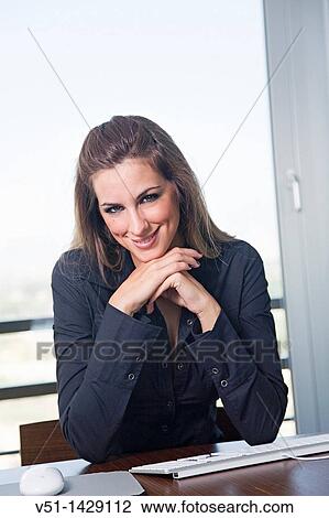 Stock Image - Portrait of a blonde woman at workplace smiling at camera. Fotosearch