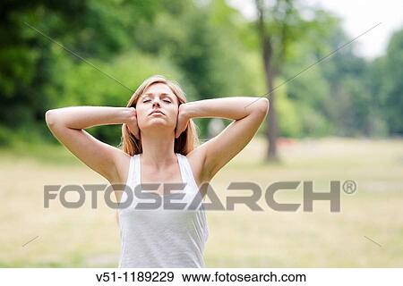 Portrait of a blonde woman covering her ears in the park View Large Photo Image Stock Photo - Portrait of a blonde woman covering her ears in the park. Fotosearch