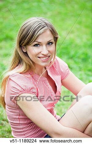 Picture - Portrait of a blonde woman sitting in the park and smiling at camera. Fotosearch