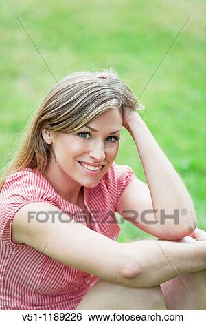 Stock Photograph - Portrait of a blonde woman sitting in the park and smiling at camera. Fotosearch