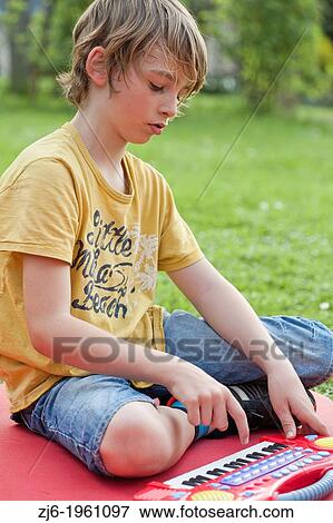 Stock Photo - Portrait of a boy with keyboard playing outdoor in the garden.. Fotosearch
